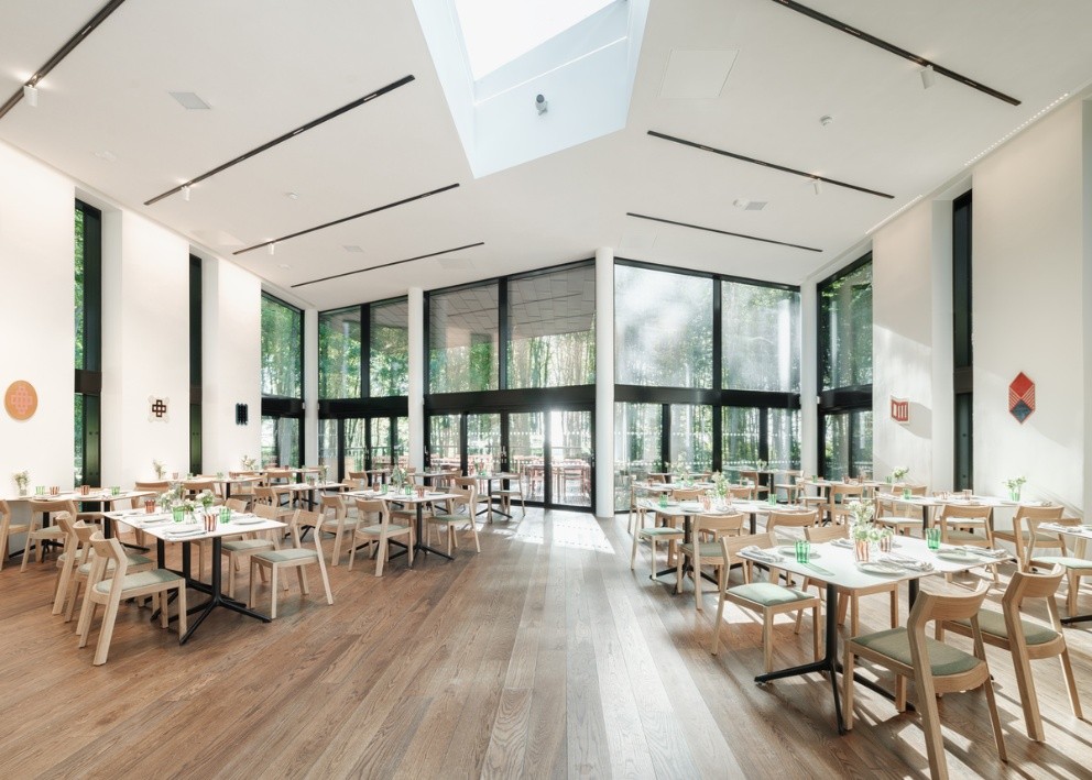 Salle lumineuse avec grandes baies vitrées, mobilier en bois clair et ambiance épurée donnant sur un jardin extérieur.