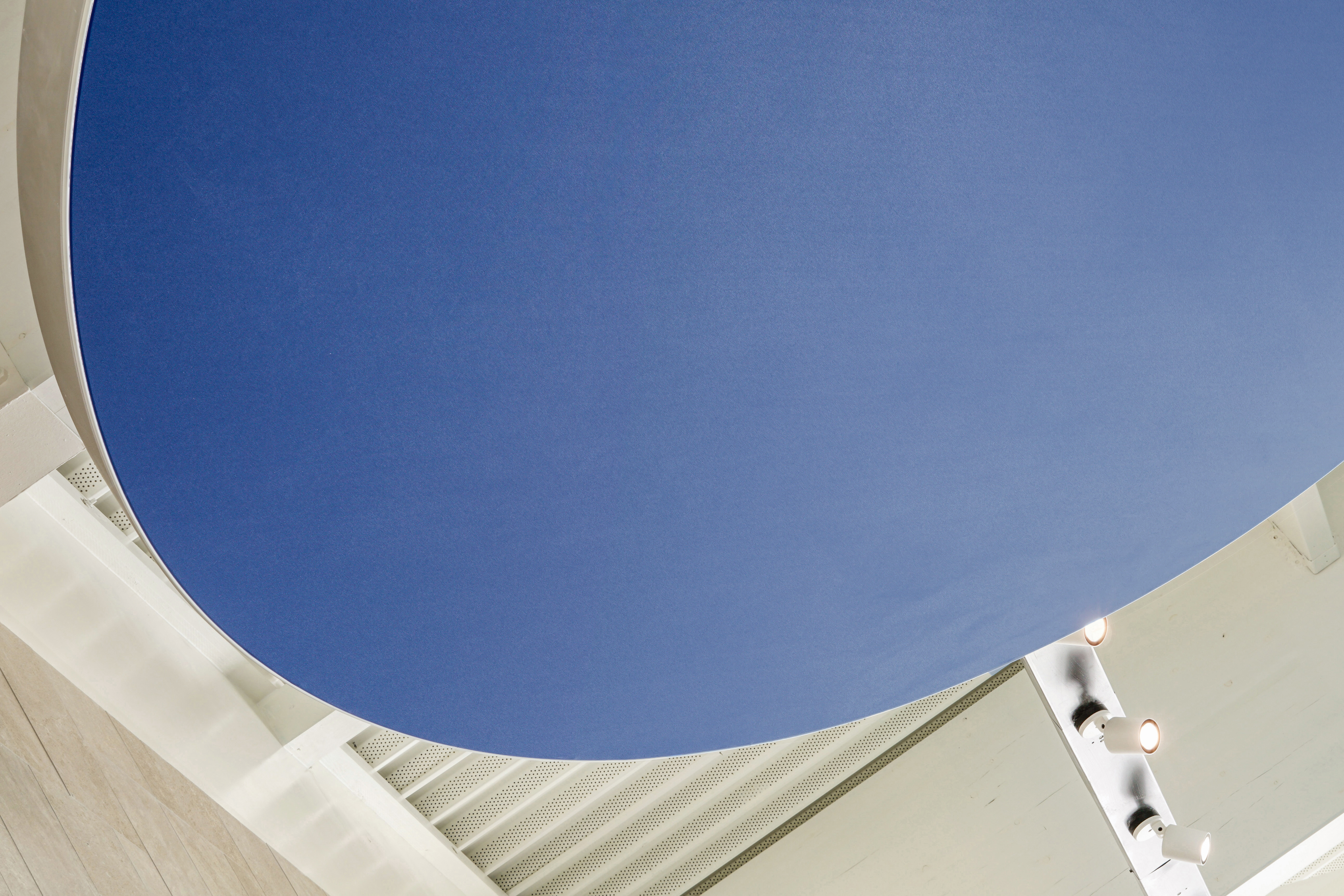 Vue rapprochée d’un plafond suspendu bleu en toile technique Ecophon Clipso™, montrant sa forme organique et sa finition lisse, avec les structures du spa visibles en arrière‑plan.