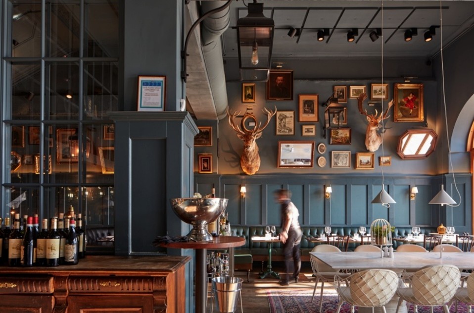 Restaurant au style vintage avec galerie de cadres sur mur bleu, trophées décoratifs et ambiance tamisée et chaleureuse.