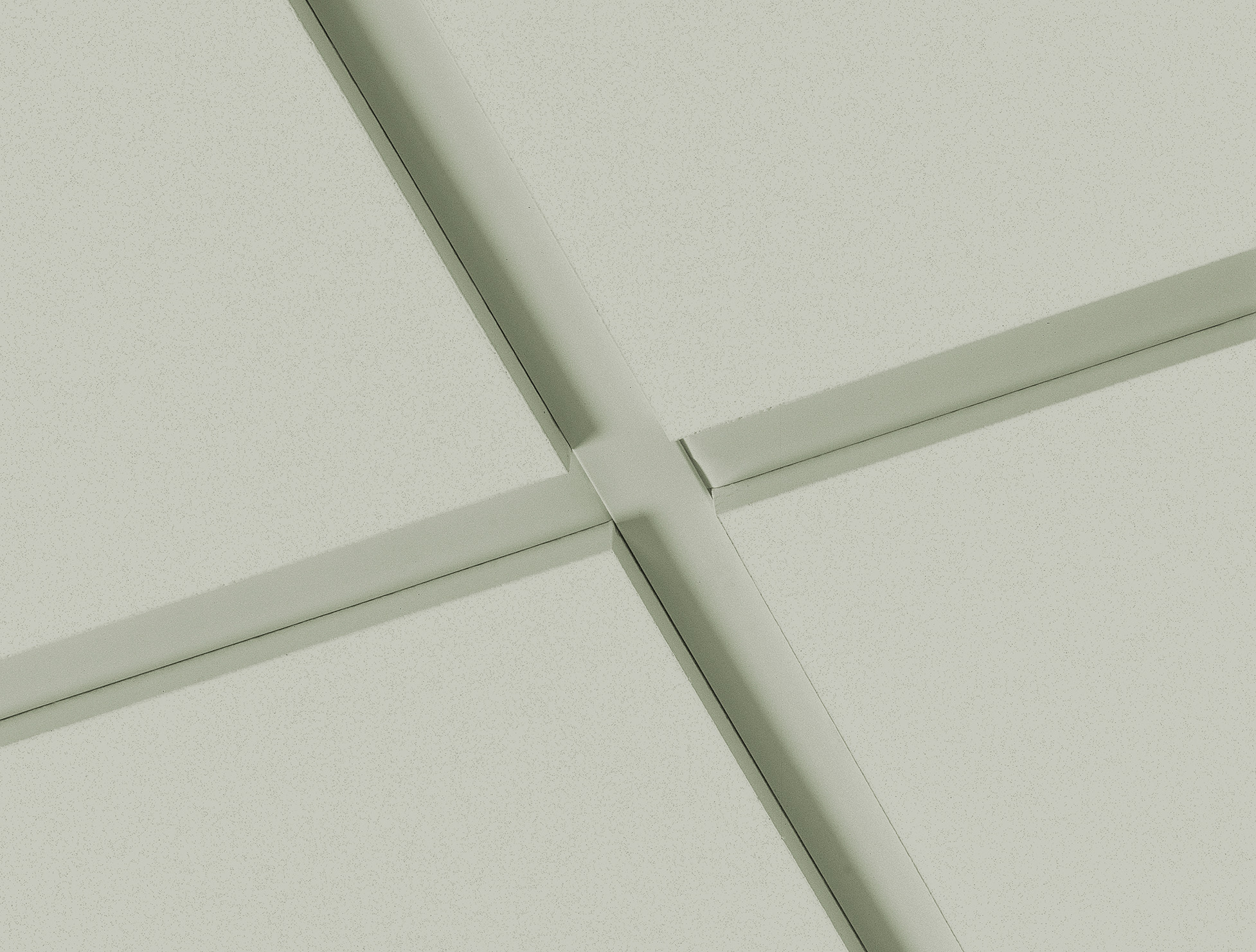 Close-up view of a light grey ceiling with intersecting metal grid lines forming square panels, typical of a suspended ceiling in an office or commercial building.