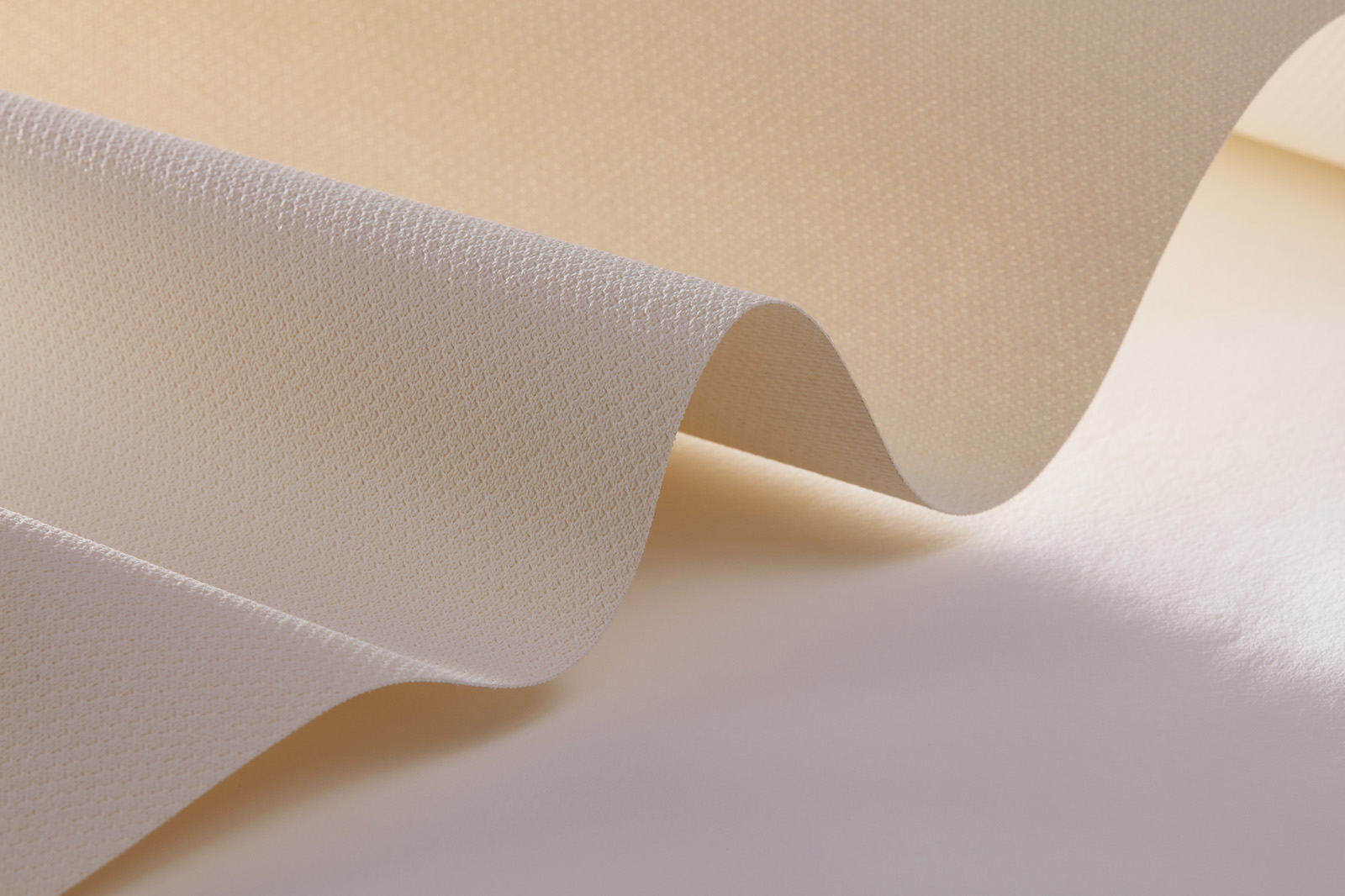 Close-up of a soft, beige fabric with a subtle wavy pattern, highlighting its texture and gentle folds. The fabric appears smooth and has a delicate sheen, catching light softly.