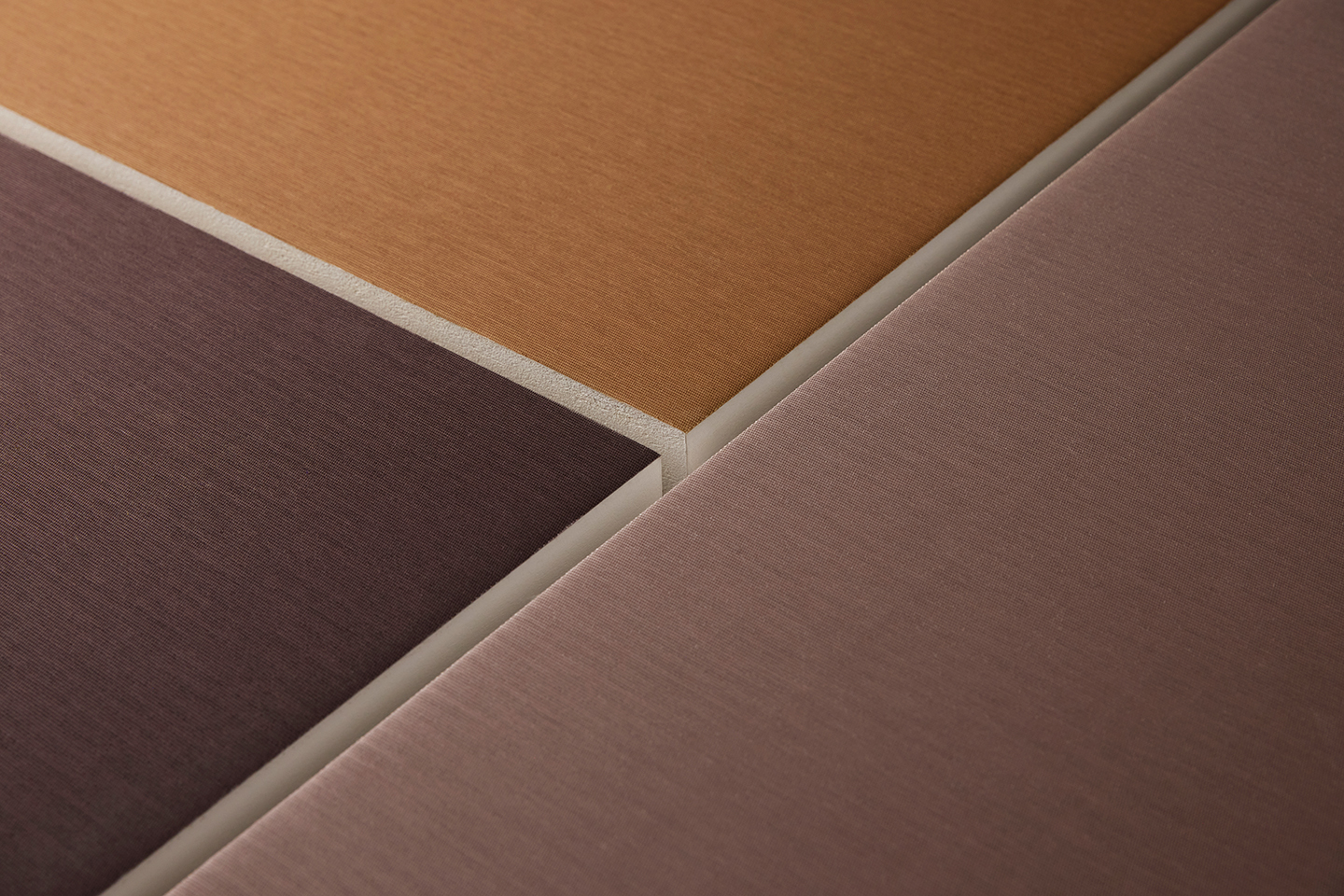 Close-up of three fabric-covered acoustic panels in warm earthy colours, showing their textured surfaces and the clean, angled edges where the panels meet.