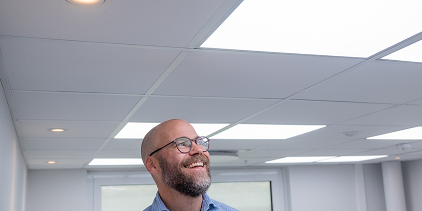 A smiling man looking up at an acoustic ceiling with integrated lighting panels