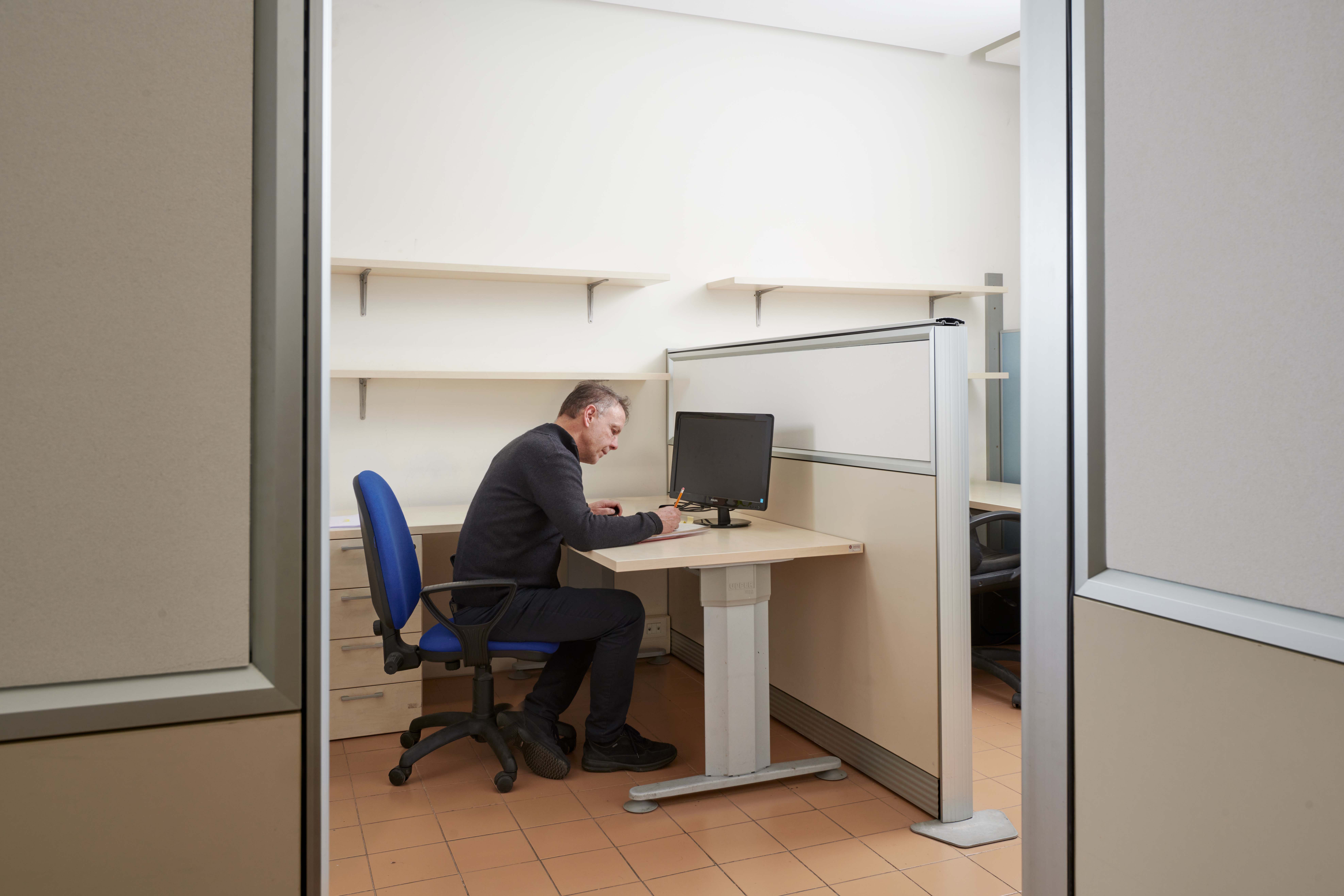 Impiegato lavora al comuputer, poggiato su una scrivania, con di fronte il pannello Akusto Screen in colorazione bianca