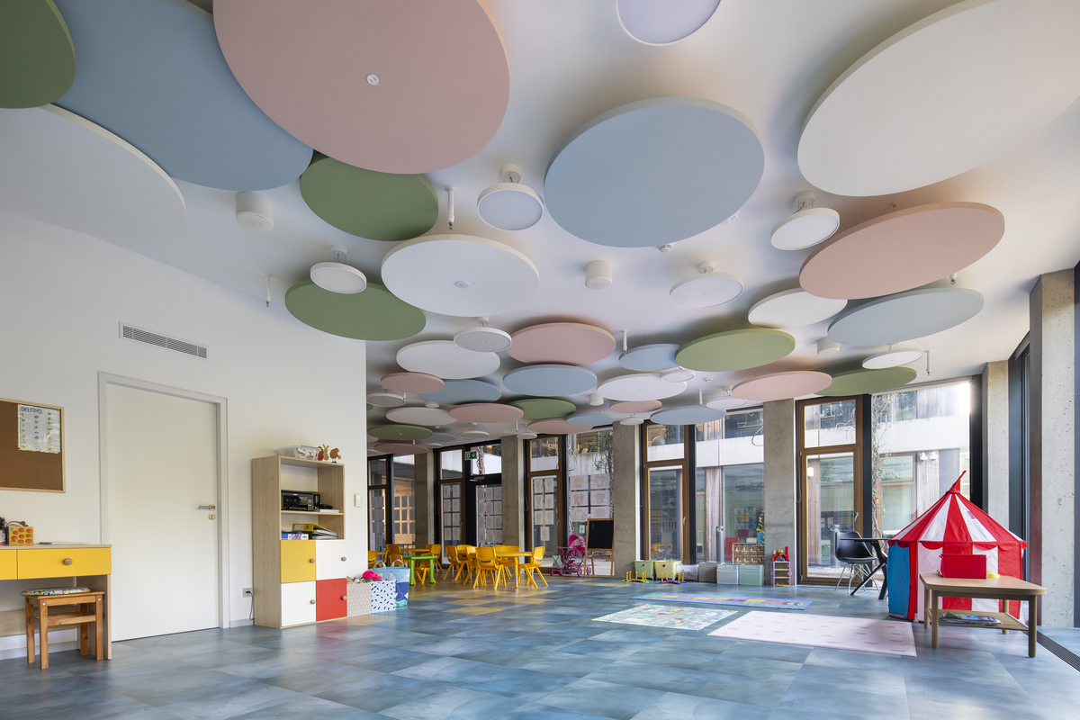 Free-hanging acoustic panels in pastel colours in large room in children's centre with colourful furniture and big windows