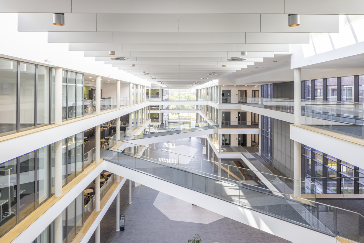 Bright, modern multi-storey building interior with large glass windows, open corridors, and multiple intersecting walkways, allowing natural light to fill the spacious atrium.
