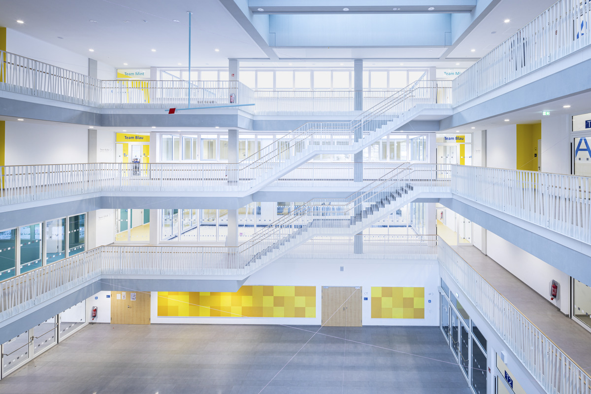White acoustic ceiling in spacious atrium with staircases and yellow details on the walls