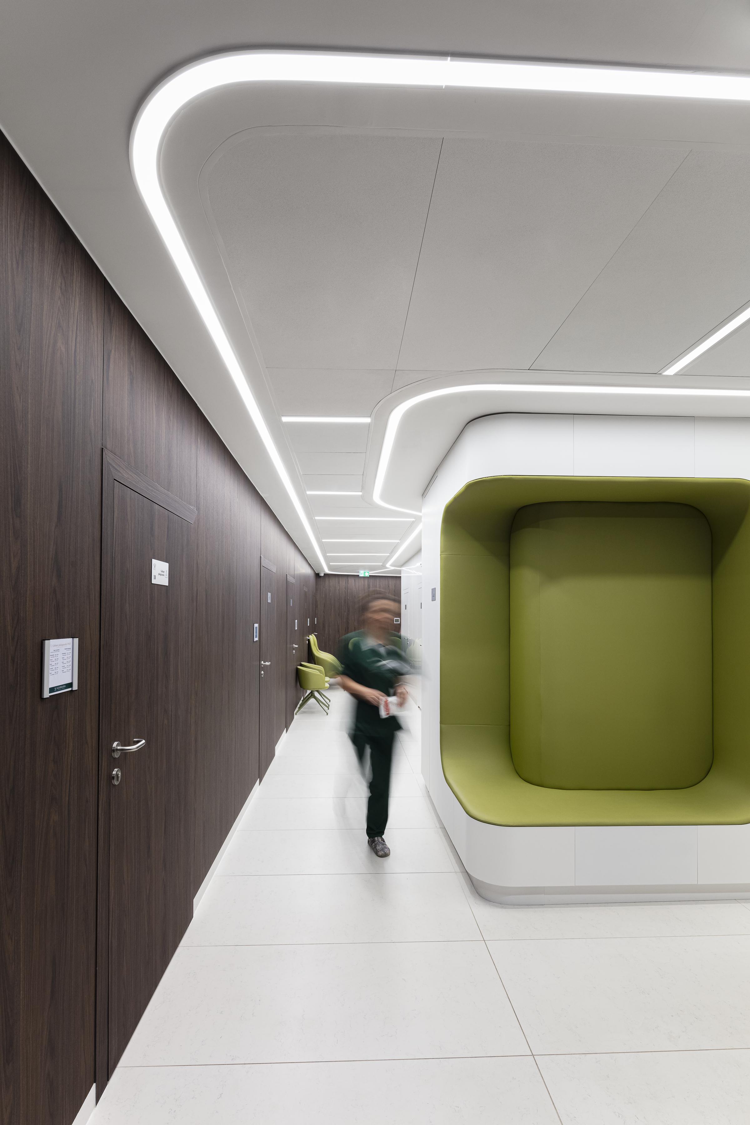 Hospital staff walking in corridor with suspended acoustic ceiling, dark brown walls and doors and a green interior detail