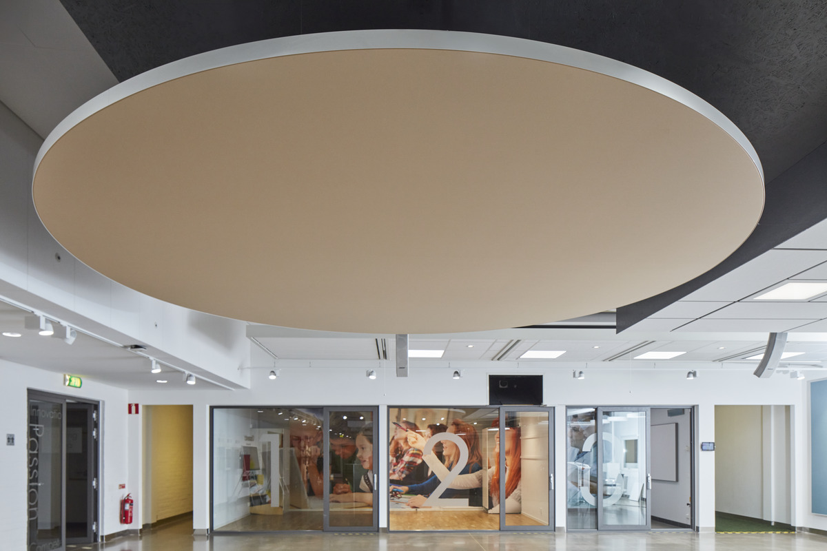 En modern interiör med en stor rund beige takpanel, glasväggar och en utställningsyta med en fototapet. Utrymmet är väl upplyst med spotlights och vita väggar.