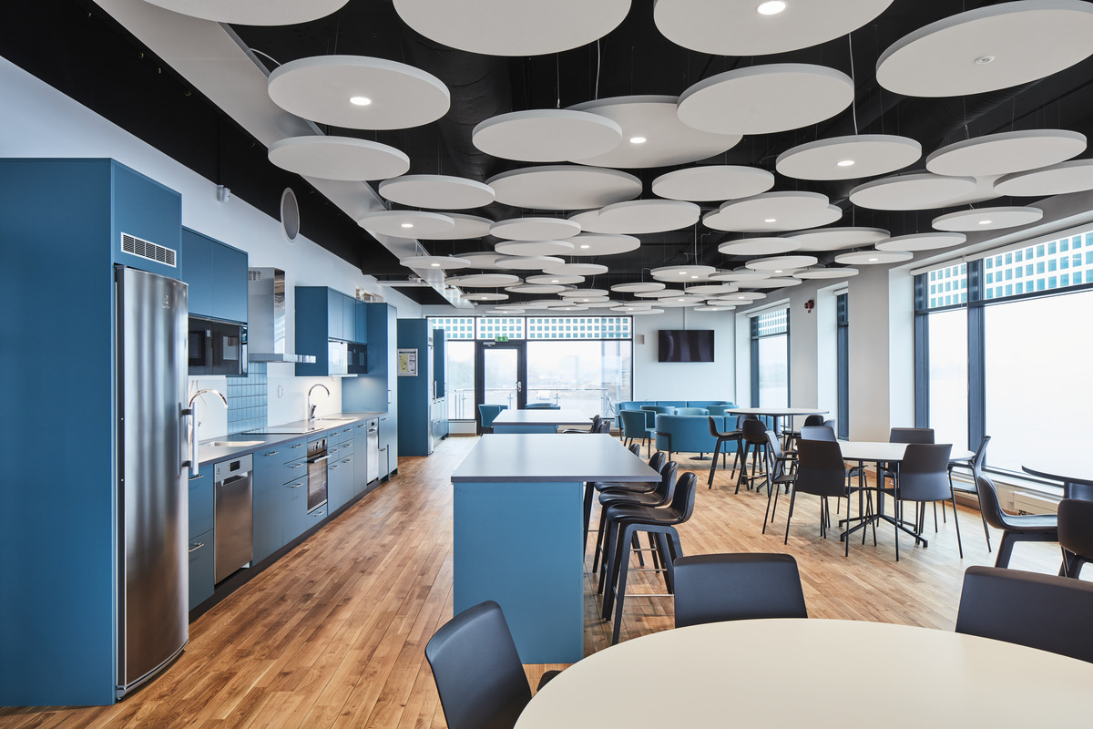 Round, free-hanging acoustic ceiling panels hanging at different levels in office kitchen and dining area with furniture and kitchen in turquoise