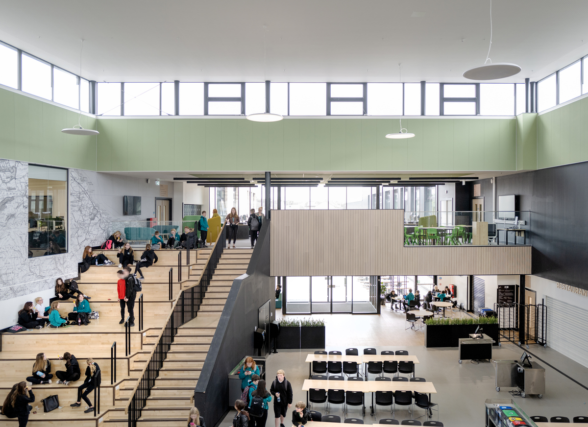 Light-green acoustic wall panels in large, spacious high school atrium with students sitting and walking in the main staircase