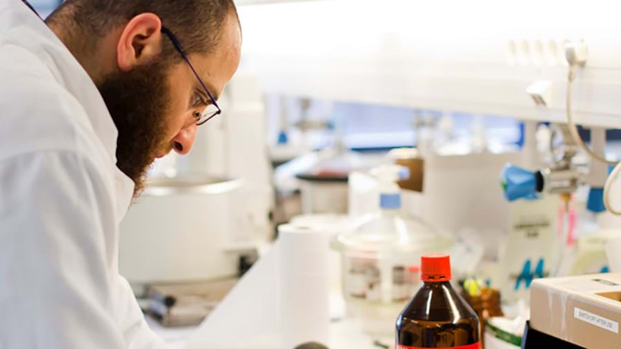 Ein Wissenschaftler mit Brille und Laborkittel arbeitet in einem hellen Labor, umgeben von Laborgeräten, Flaschen und wissenschaftlichen Instrumenten.