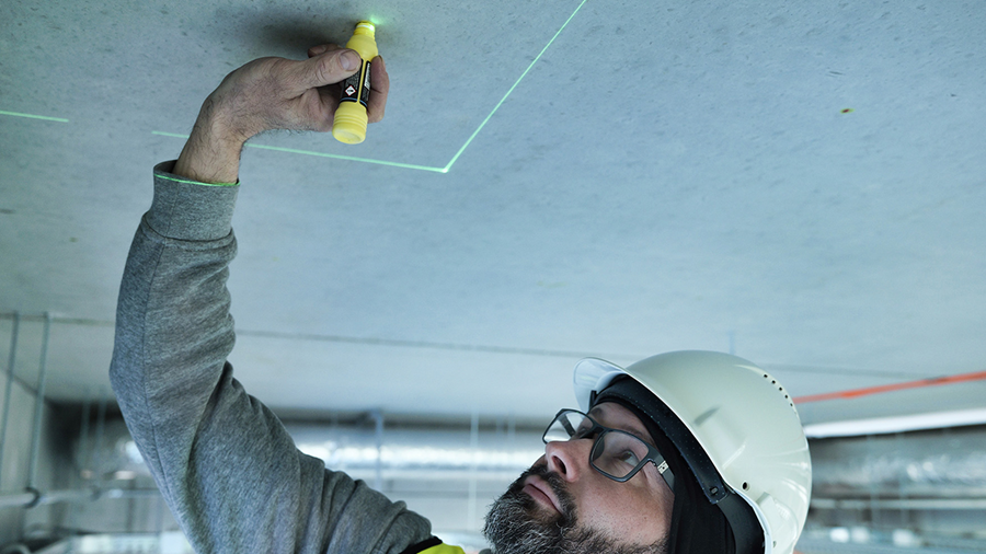 Technician marking ceiling based on green laser projection lines guiding precise mounting positions