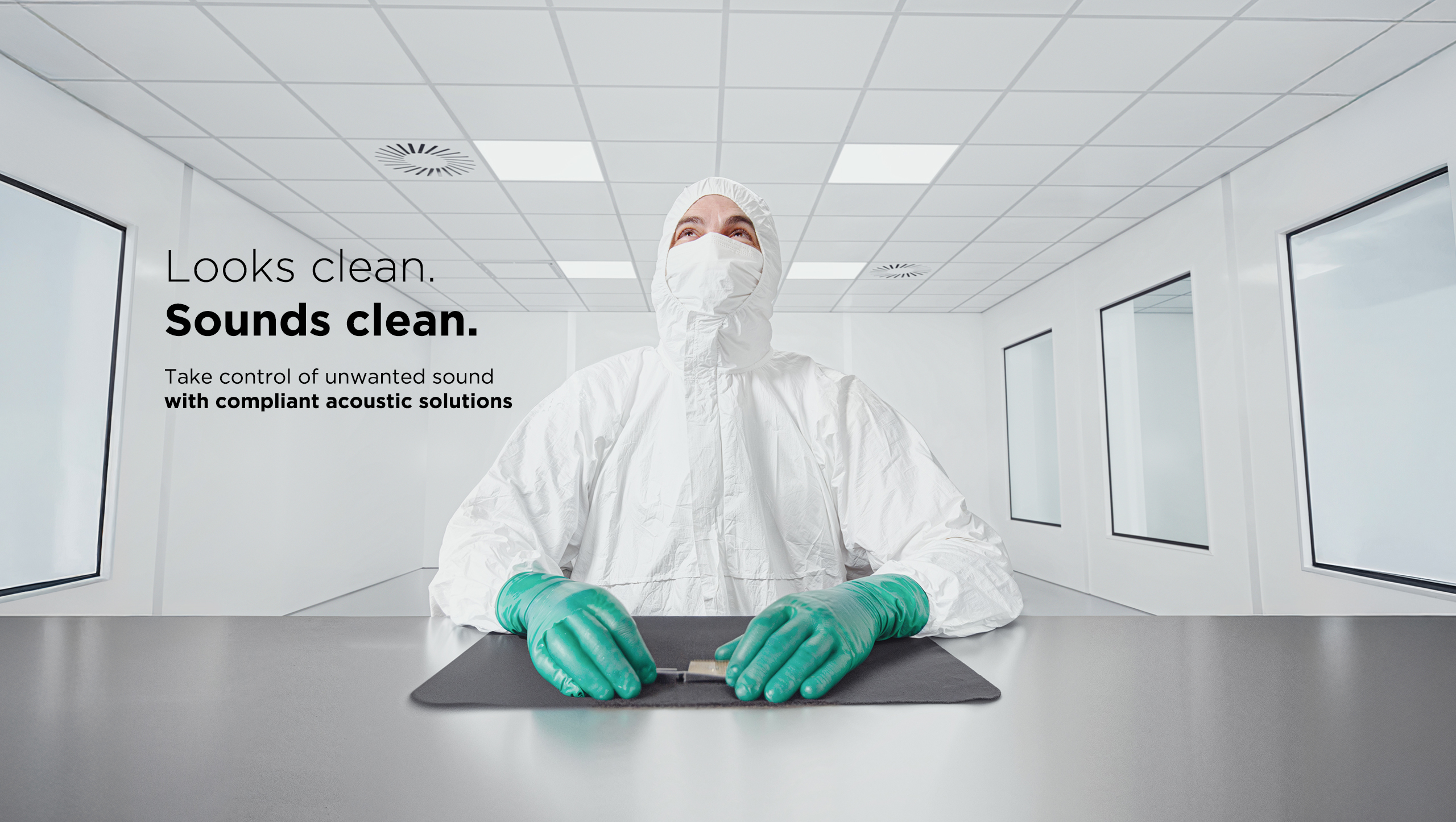 A person in a white cleanroom suit and green gloves sits at a table in a bright, sterile laboratory. Text reads: Looks clean. Sounds clean. Take control of unwanted sound with compliant acoustic solutions.