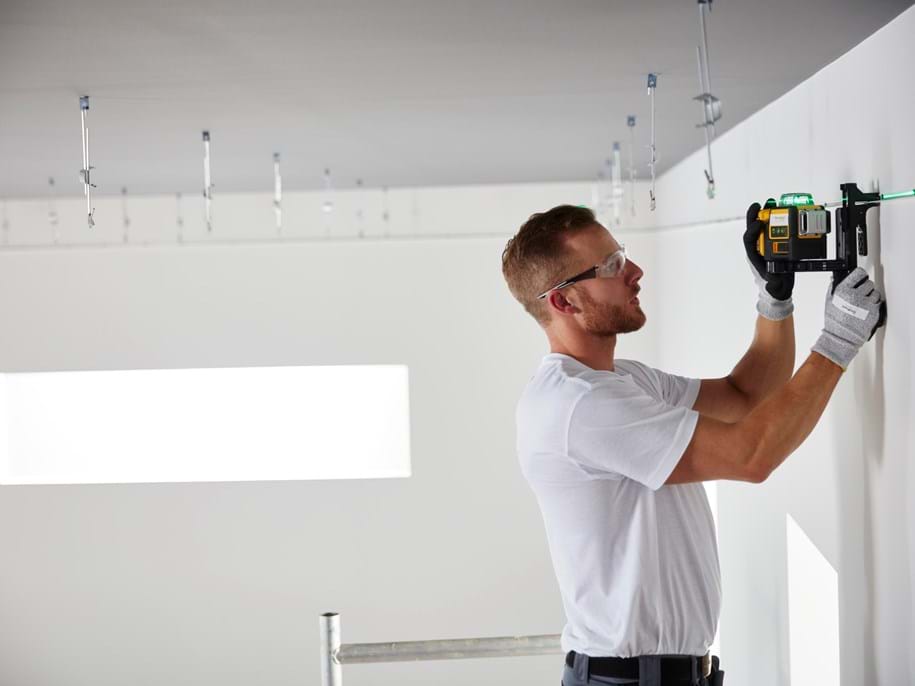 Instalator mierzy puste pomieszczenie, przygotowując się do instalacji sufitu.