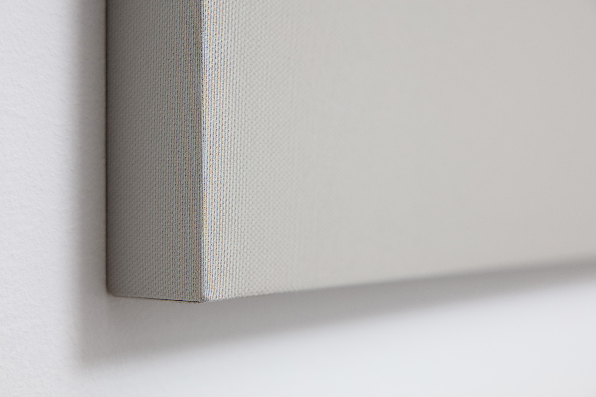 Close-up of a beige canvas stretched over a wooden frame, hanging on a white wall. The texture of the canvas is visible, and the image captures the edge and part of the front surface.