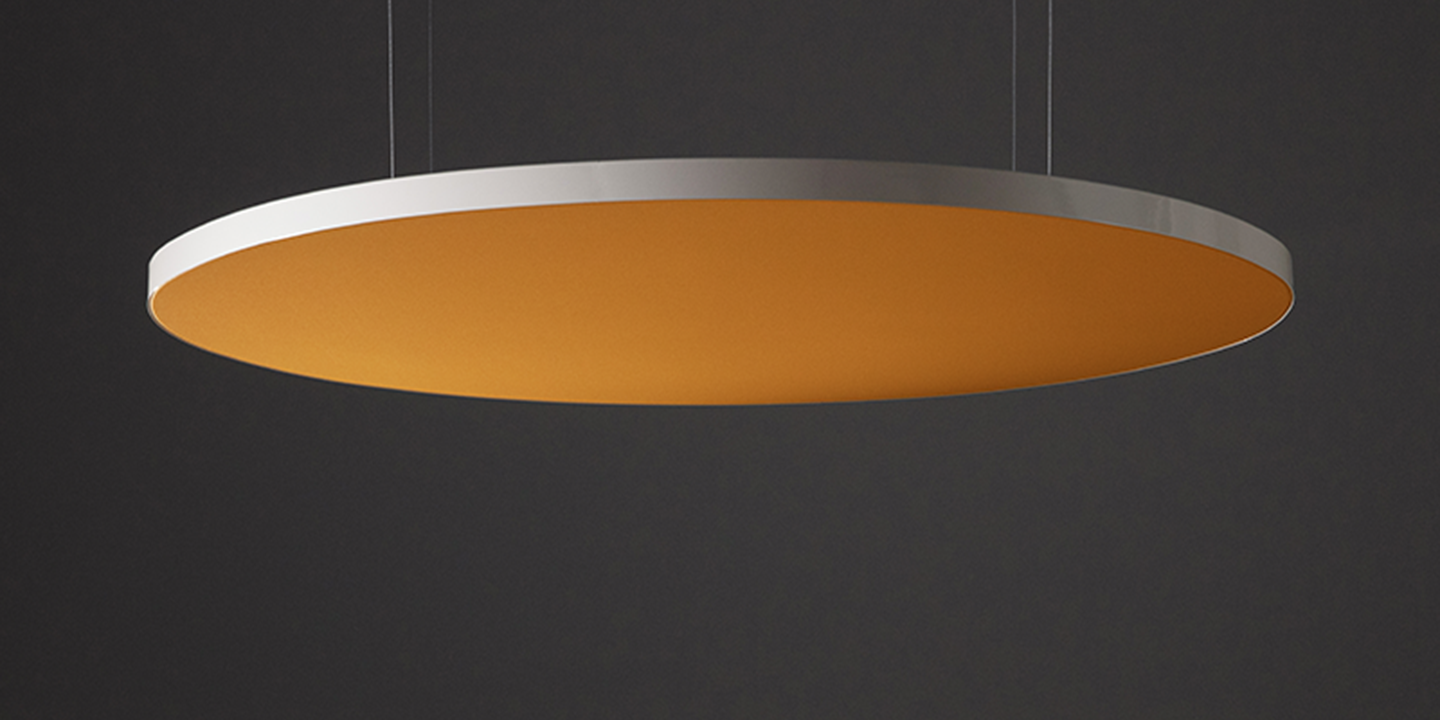 A modern, circular orange and silver acoustic panel hangs against a dark background, suspended by thin cables. The underside is orange, contrasting with the sleek silver edge.