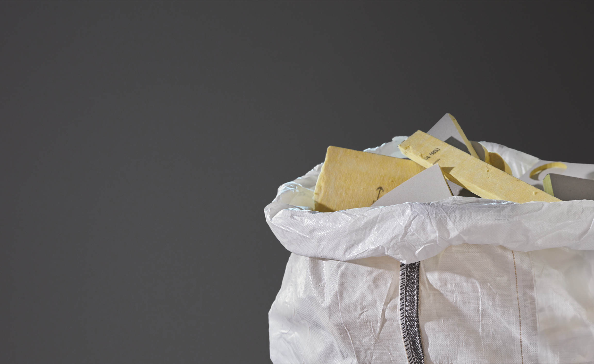 Close-up of a white plastic bag filled with used acoustic glasswool panels