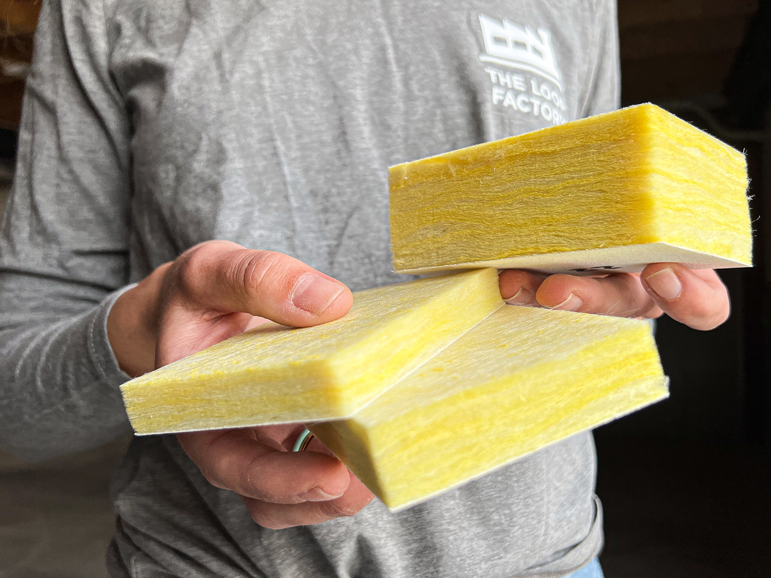 A person wearing a grey shirt holds three yellow insulation foam panels, each rectangular and thin, stacked in one hand.