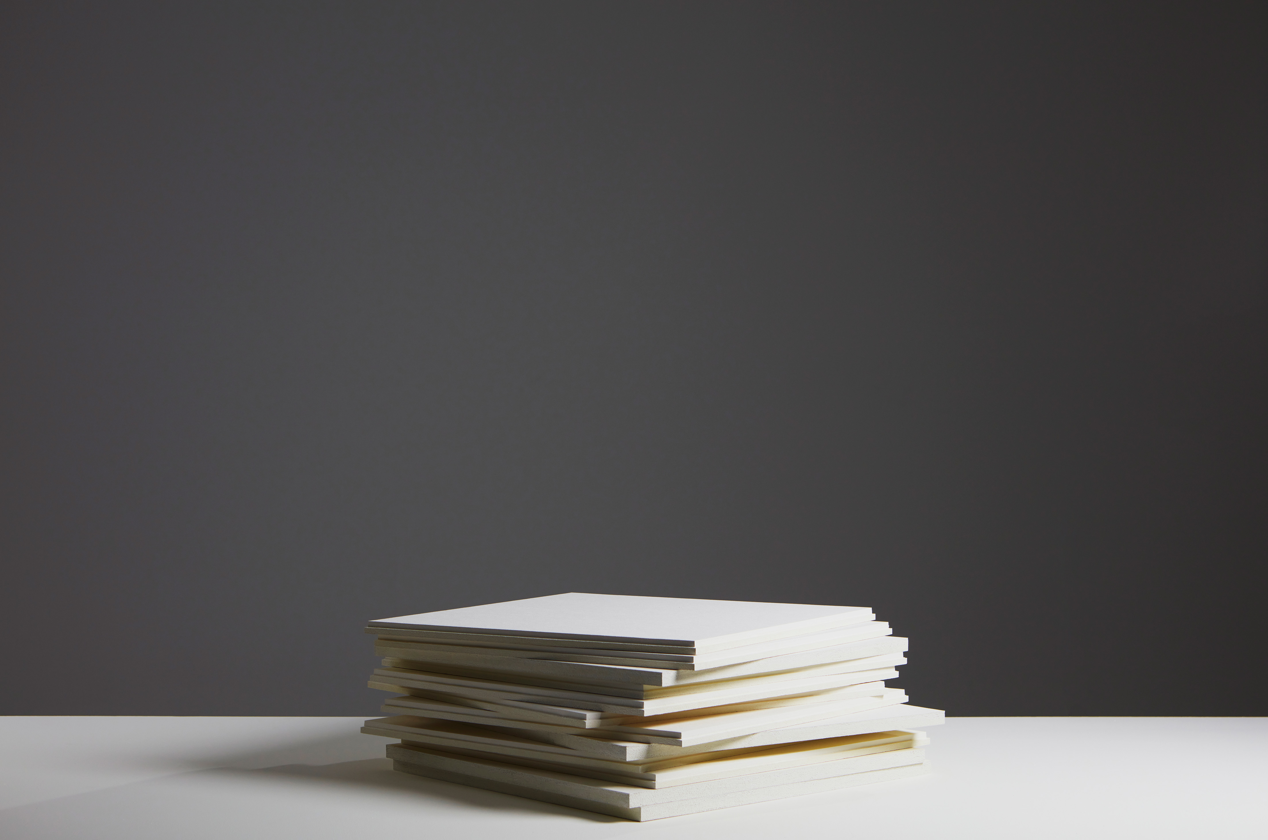 Stack of white acoustic panels on a white surface against a dark background