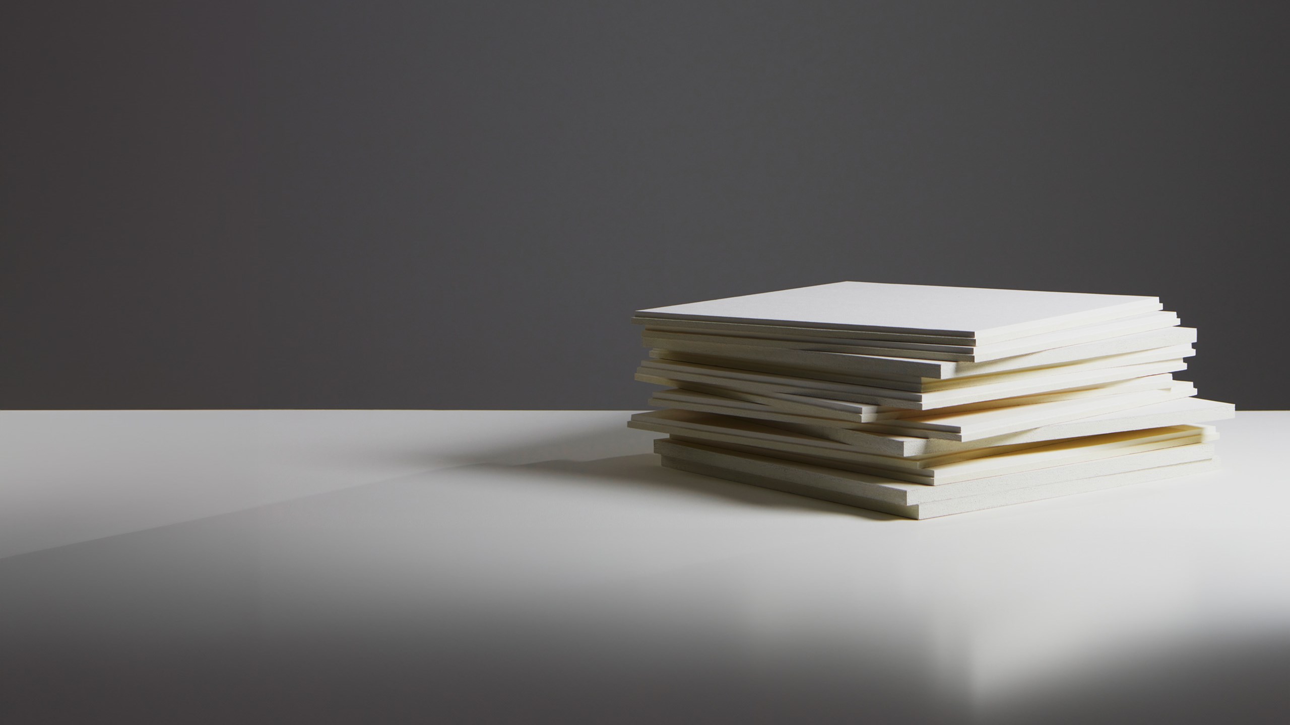 A pile of white acoustic panels lying on a white surface and a dark grey background